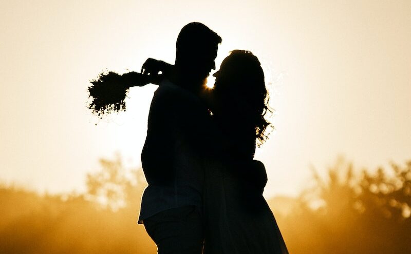Side view silhouettes of happy young couple hugging each other while relaxing on sandy beach during date at sunset
