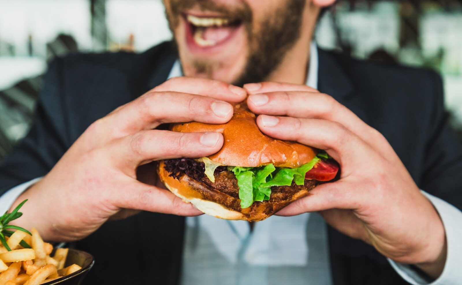 person holding burger bun with vegetables and meat