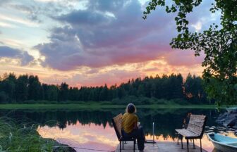 man in black jacket sitting on brown wooden bench near lake during daytime