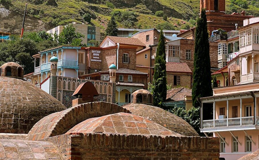 Scenic view of the historic sulfur baths in Tbilisi, Georgia, surrounded by colorful houses and lush hills.
